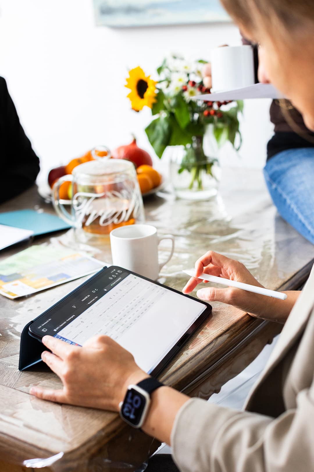 Pflegekraft bei einem Hausbesuch, nutzt Tablet für Dokumentation, umgeben von Blumen und einem ruhigen Gesprächstisch