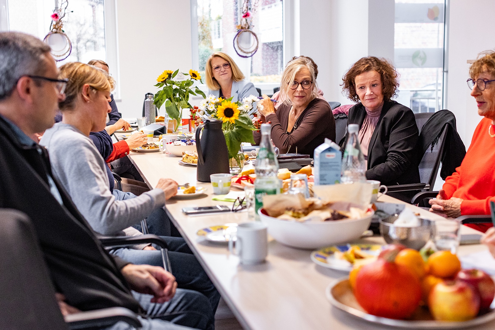 Ein Team des PKD Coesfeld sitzt bei einem gemeinsamen Treffen in einem hellen Raum, umgeben von Blumen und Obst.